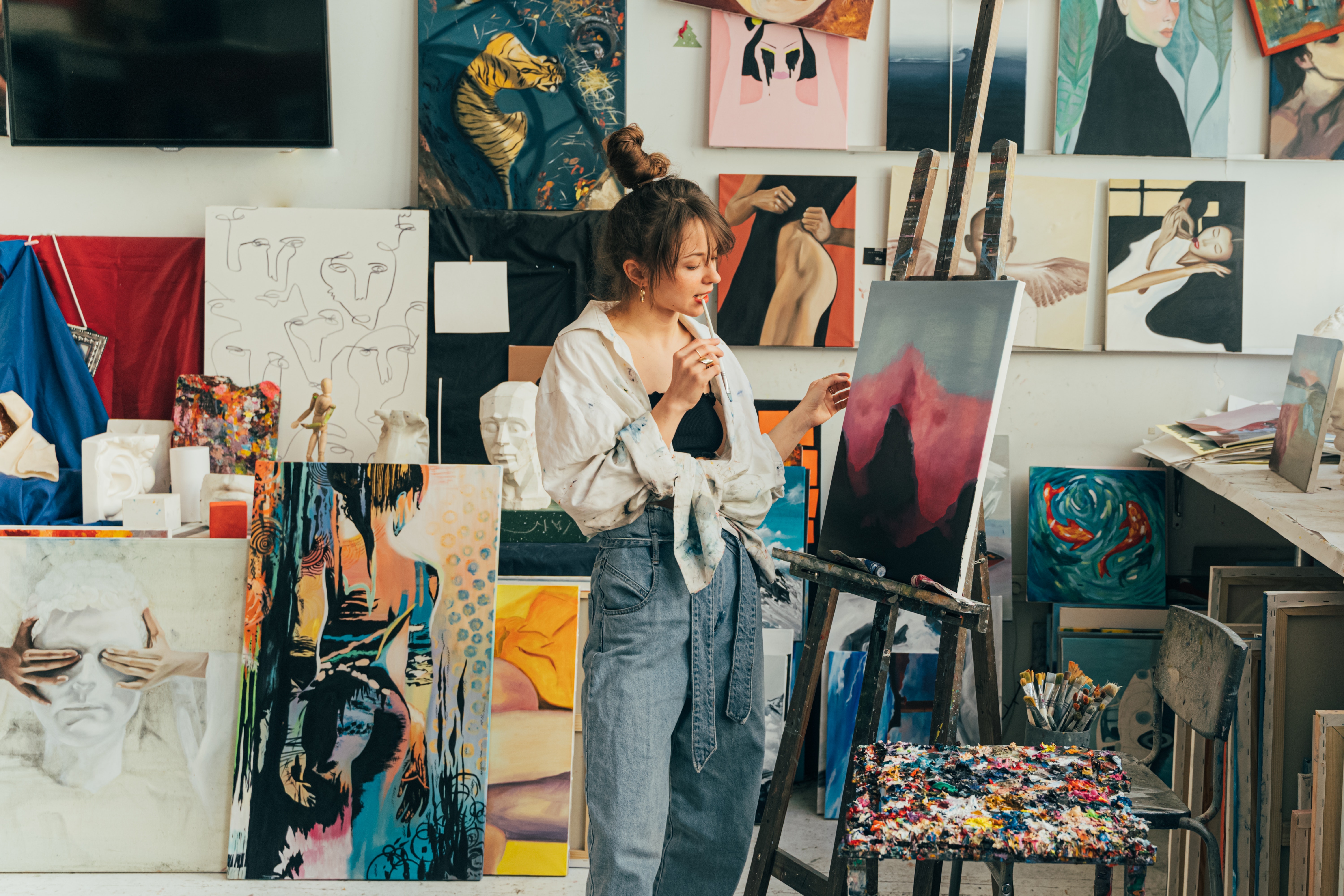 an artist painting on a canvas, surrounded by canvases
